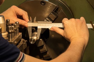 Torna makinesinde Vernier Caliper tarafından metal şaft parçalarının boyutlarını ölçen makine operatörü. Dönüş makinesinin kalite kontrolü. 