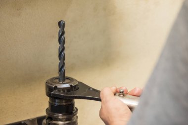 İşçi matkap aletini tutucuya sıkılaştırır. Anahtarla klempleme aracı.
