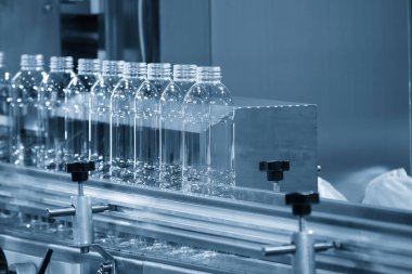 Açık mavi sahnede içme suyu üretim sürecinin yüksek teknolojisi. Taşıma bandındaki boş içme suyu şişelerini doldurmak için.. 