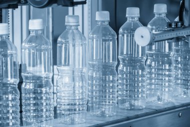Açık mavi sahnede içme suyu üretim sürecinin yüksek teknolojisi. Taşıma bandındaki boş içme suyu şişelerini doldurmak için.. 