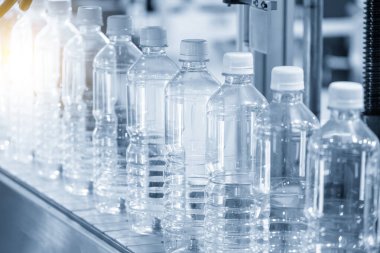 Açık mavi sahnede içme suyu üretim sürecinin yüksek teknolojisi. Taşıma bandındaki boş içme suyu şişelerini doldurmak için.. 