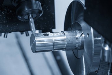 Dönme dolap makinası açık mavi sahnede mili mille keserek metal şaft parçalarını kesiyor. CNC turn-mill makinesiyle çalışan yüksek teknoloji metali.