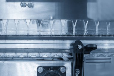 Boş içme suyu şişeleri, doldurmak için üstteki taşıma bandında asılı. İçme suyu üretim sürecinin yüksek teknolojisi. 