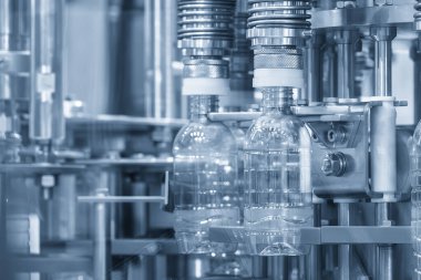 Taşıyıcı banttaki boş içme suyu şişeleri mavi tonda doldurmak için. İçme suyu üretim sürecinin yüksek teknolojisi. 