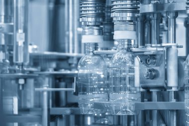 Taşıyıcı banttaki boş içme suyu şişeleri mavi tonda doldurmak için. İçme suyu üretim sürecinin yüksek teknolojisi. 