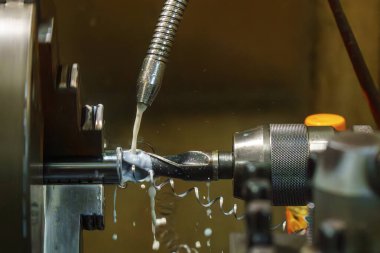 Sıvı soğutucu metoduyla makineyi döndürme işlemi. Açık mavi sahnede torna makinesi ile metal çalışma süreci.