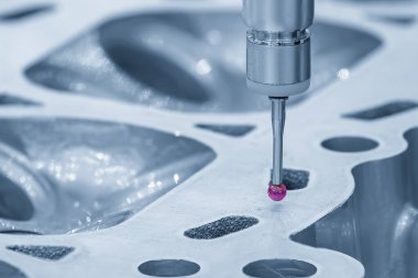 Açık mavi sahnede alüminyum silindir kafa parçalarını ölçen çok eksenli CMM makinesi. Çoklu eksen CMM makinesi ile otomotiv parçalarının kalite kontrolü.