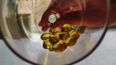 Golden pills omega 3 fall in glass medicine healthcare concept white background close up