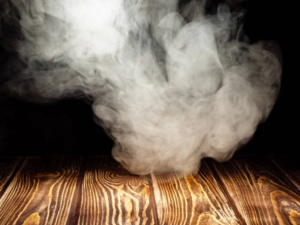Siyah arka planda, tahta bir tahtanın üzerinde yoğun beyaz bir duman bulutu.