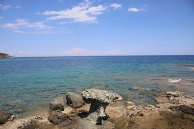 Güzel deniz ve gökyüzü ile kayalık kumlu sahil.