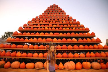 10 years girl in witch hat with pumpkin pyramid in background clipart