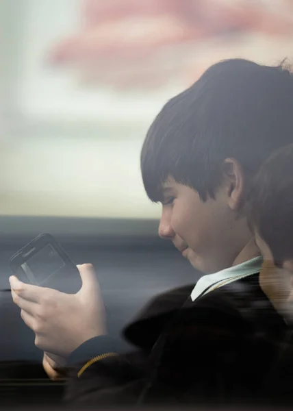 スマートフォンで遊んでいる車の窓ガラスを通して制服を着た子供たちの肖像画を閉じます サイドビュー — ストック写真