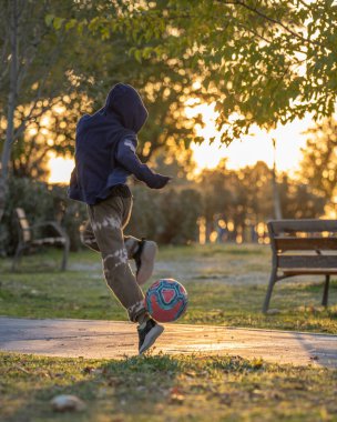 Genç, beyaz bir çocuk doğada gün batımında futbol topuyla numara yapıyor. Kentsel şehir yaşam tarzı açık hava kavramı.