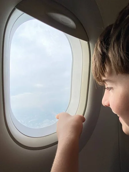 Caucasian boy looking outside of airplane window and pointing with the finger.