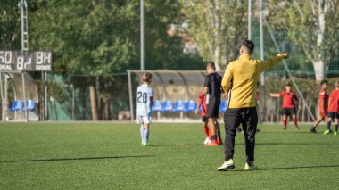 Futbol koçu maç boyunca çocuklara futbol takımı hakkında talimatlar veriyor.