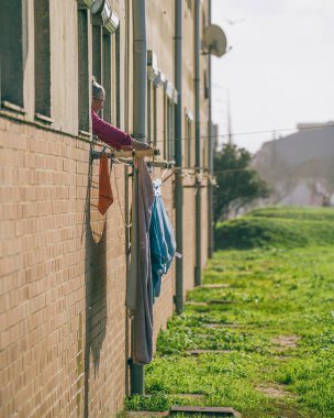 Old woman tends laundry hanging in the Portuguese sunshine in Espinho, Portugal. January 2023.