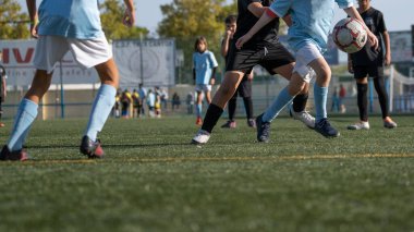 Young soccer players running fast and kicking white football ball. Youth footballers compete in tournament match. Soccer athlete kicking ball. School sports competition.