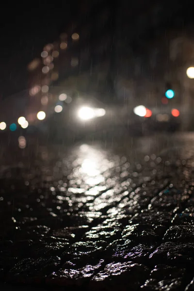 车辆前灯在雨中闪烁着模糊的低角度视图 夜间在湿透的鹅卵石上反射 — 图库照片
