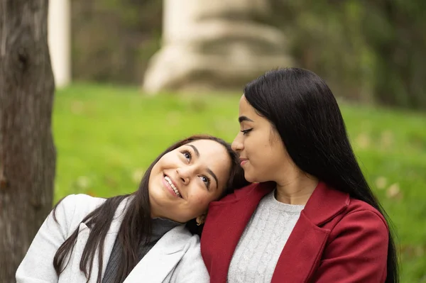 Portrait of smiling lesbian latin women relaxed together outdoors sitting on the grass.