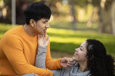 Mutlu Latin kadın erkek arkadaşının yüzüne dokunuyor ve fotokopi aletiyle çimlerin üzerinde oturuyor..