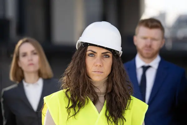 Portrait of serious woman construction architect with customer executives behind. Woman leadership and management concept.