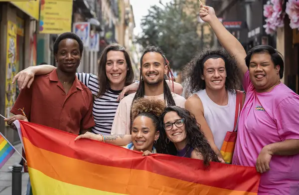 Group of happy LGBTQ people are posing with a rainbow flag before a gay parade MADO in Madrid city.