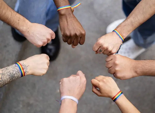 Gökkuşağı bilezikleriyle birlik gösteren çok ırklı homoseksüel grupların yumrukları ya da kapalı elleri.