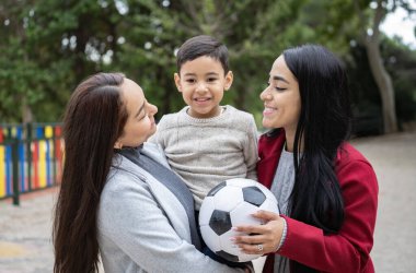 Oğullarını futbol oyuncağıyla tutan Latin lezbiyen çiftin portresi. Çeşitlilik ve LGBT Ailesi.