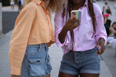 İki tanınmayan etnik çeşitlilikte genç kadın bir arada duruyor ve akıllı bir telefon arıyorlar..