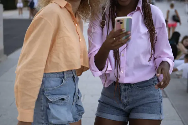 İki tanınmayan etnik çeşitlilikte genç kadın bir arada duruyor ve akıllı bir telefon arıyorlar..