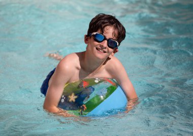 Havuzda şişme topla eğlenen genç bir çocuğun portresi..