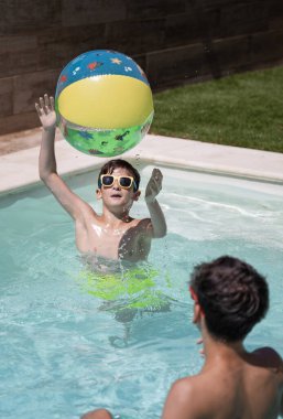 Çocuklar havuzda şişme topla oynuyorlar..