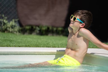 Havuzda oturup fotokopi alanı ile güneşlenen bir çocuğun yan görüntüsü..
