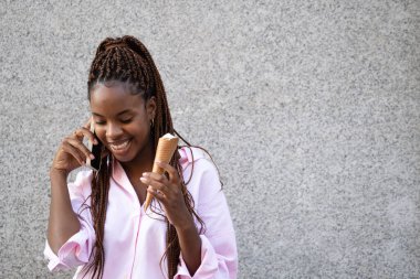 İş dünyası genç Afrikalı Amerikalı kız telefonla konuşurken gülümsüyor ve elinde dondurma tutuyor..