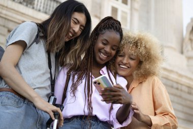 Çoklu etnik çeşitliliğe sahip genç turistlerin gülümsemeleri ve akıllı telefonlarına bakmaları düşük açı.,