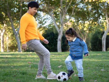 Dominikli bekar baba ve oğul bir futbol topuyla parkta oynuyorlar..