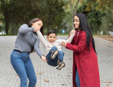 İki lezbiyen anne parkta oğullarını havaya kaldırıp döndürerek eğleniyorlar.
