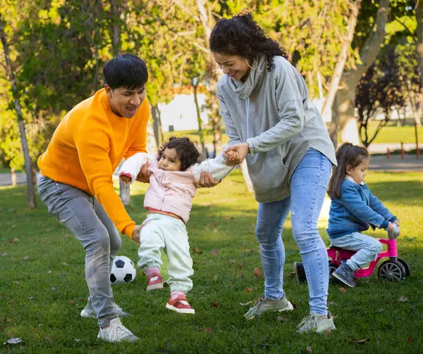 Güneşli bir günde, İspanyol ailenin parkta birlikte vakit geçirmesini ön plana çıkarmak. Ebeveynler küçük kızlarını taşıyorlar..