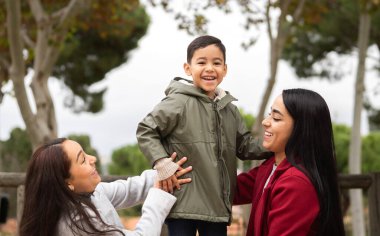Oğullarıyla birlikte parkta eğlenen İspanyol anneler ön planda. Lgbt aile kavramı.