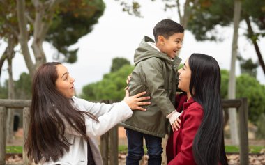 Başka bir kadın bakarken bir kadın kucağında bir çocuk tutuyor. Sahne sıcak ve sevgi dolu.
