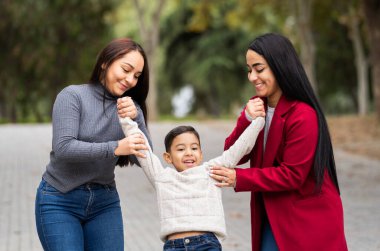 Üç kadın ve bir çocuk parkta birlikte oynuyorlar. Oğlan beyaz bir gömlek giyiyor ve kadınlar gri ve kırmızı giysiler giyiyor. Sahne mutlu ve neşeli.