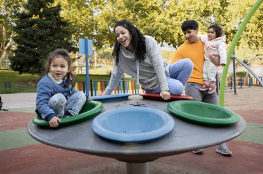 Dört kişilik bir aile dört farklı renkli kaseyle yuvarlak bir oyun yapısında oynuyor. Çocuklar bir oyun parkında ebeveynleriyle birlikte gülüyor ve eğleniyorlar. Sahne mutlu ve neşeli.