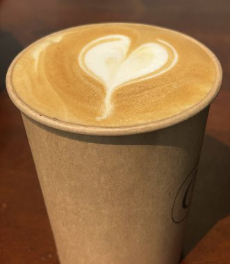 Kapuçino, karton bir bardakta, ahşap bir masada duruyor.