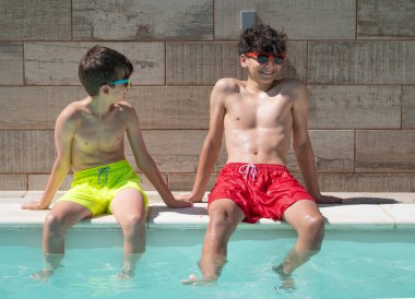 İki genç çocuk bir yüzme havuzunun kenarında oturuyor, yaz tatilinin tadını çıkarıyorlar.