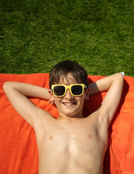Güneş gözlüklü, dışarıda havluyla rahatlayan gülümseyen çocuk.