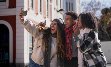 Bir grup genç turist kışın bir kenti ziyaret ederken komik surat ifadeleri takınarak selfie çekiyorlar.