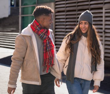 Kış kıyafetleri giyen mutlu çoklu etnik çift açık havada yürüyüş yapıyor..