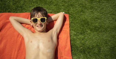 Güneş gözlüklü, gülümseyen çocuk güneşli bir günde dinleniyor.