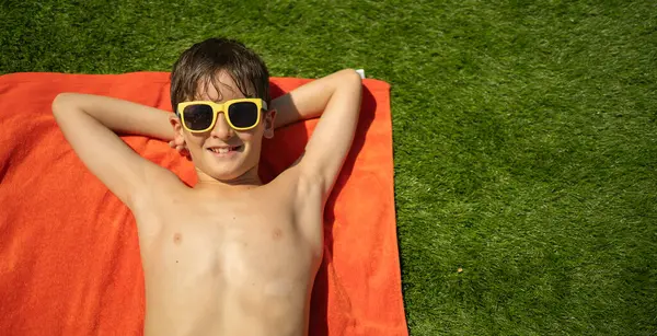 Güneş gözlüklü, gülümseyen çocuk güneşli bir günde dinleniyor.