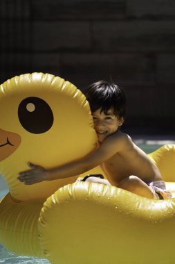 Gülümseyen çocuk yaz boyunca yüzme havuzunda yüzen dev, şişme sarı ördeğe sarılıyor..